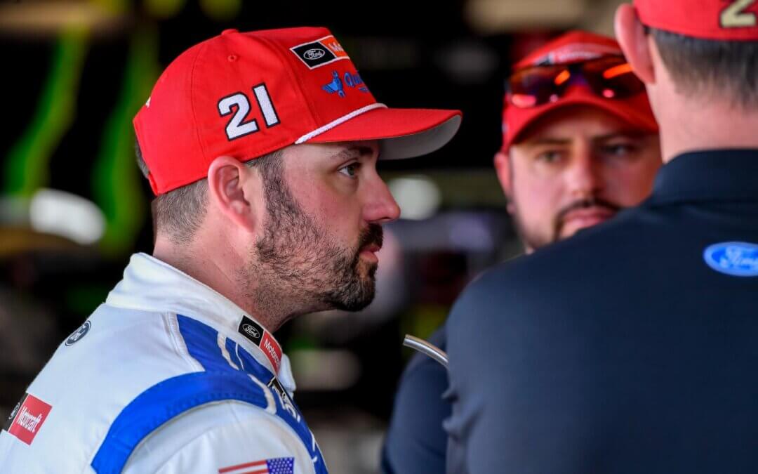 Candid side view of Josh Berry wearing a red 21 hat speaking with team members