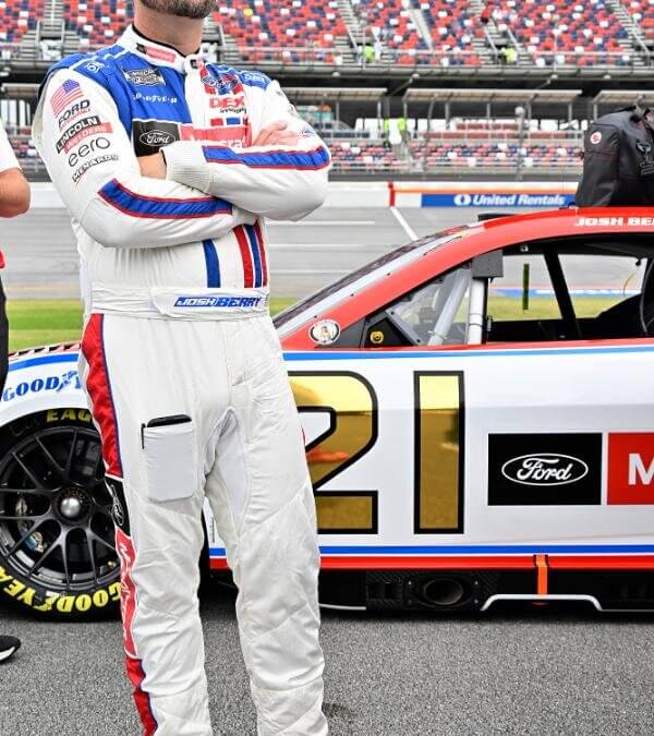 Josh Berry wearing sunglasses and standing with arms crossed in from of his number 21 NASCAR