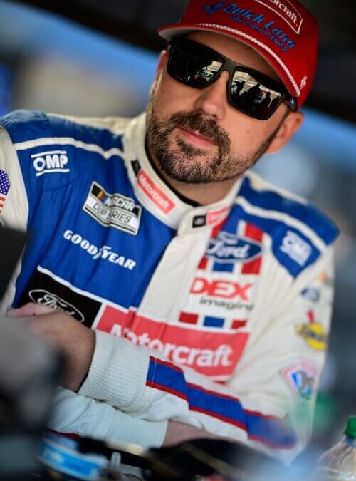 Close up portrait of Josh Berry in sunglasses and his racing suit arms crossed leaning