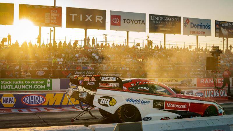 Funny car on track with the low sunlight coming through the bleachers