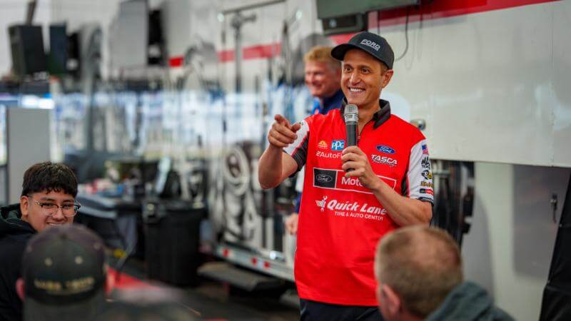 Tasca in a motorcraft shirt holding a microphone speaking