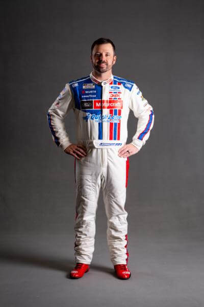 Josh Berry with hands on hips in his racing suit on a photoshoot background of grey
