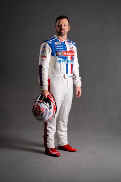 Josh Berry in his race suit on a grey background holding his race helmet down in one hand