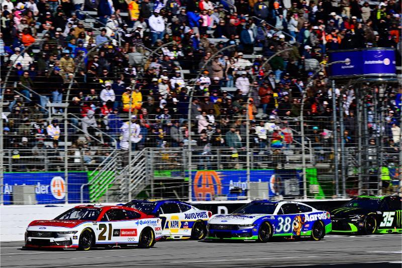Dark shot of cars on the track with the bleachers full of fans