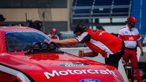 Crew member leaning onto the hood of the car going in for a fist bump through the window